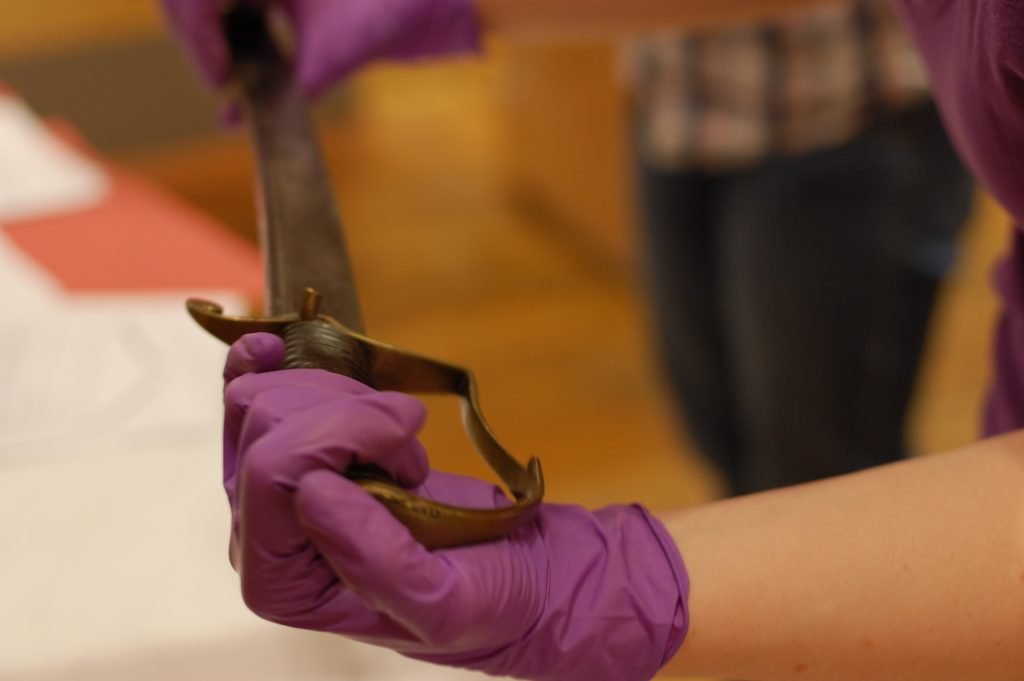 Close-up of someone wearing purple conservation gloves holding an antique sword.